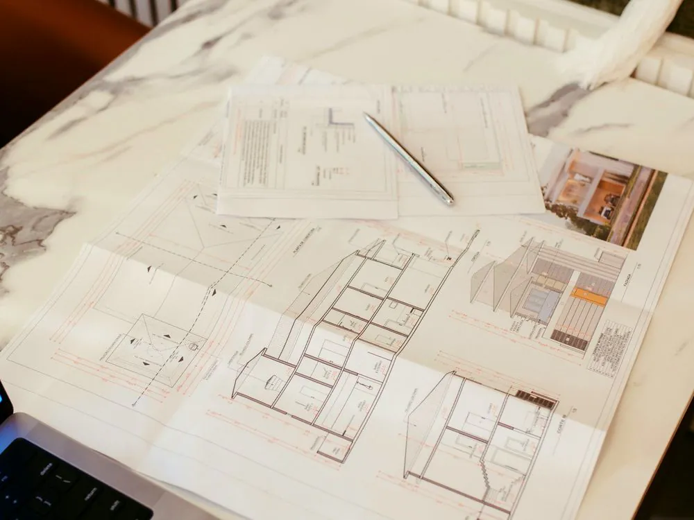 A plan set laid out on a desk beside a laptop during system design