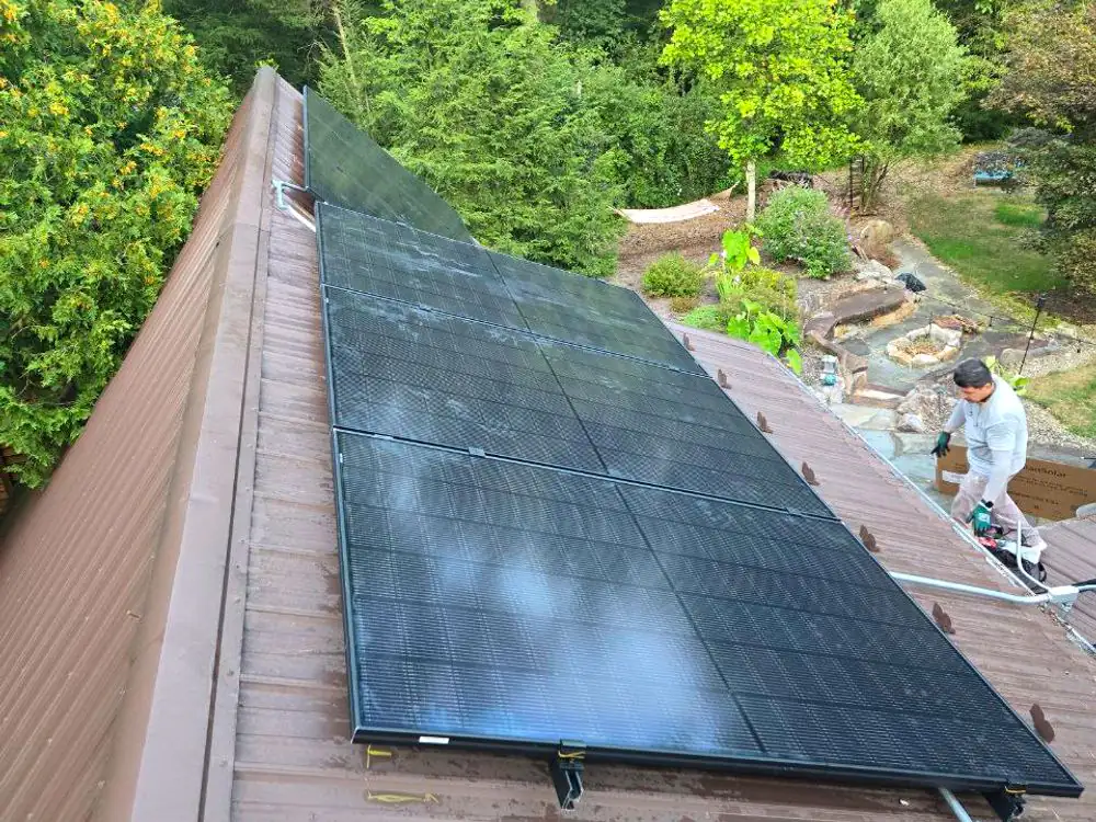 A finished run of solar modules along a bronze metal roof, with the installer still on site